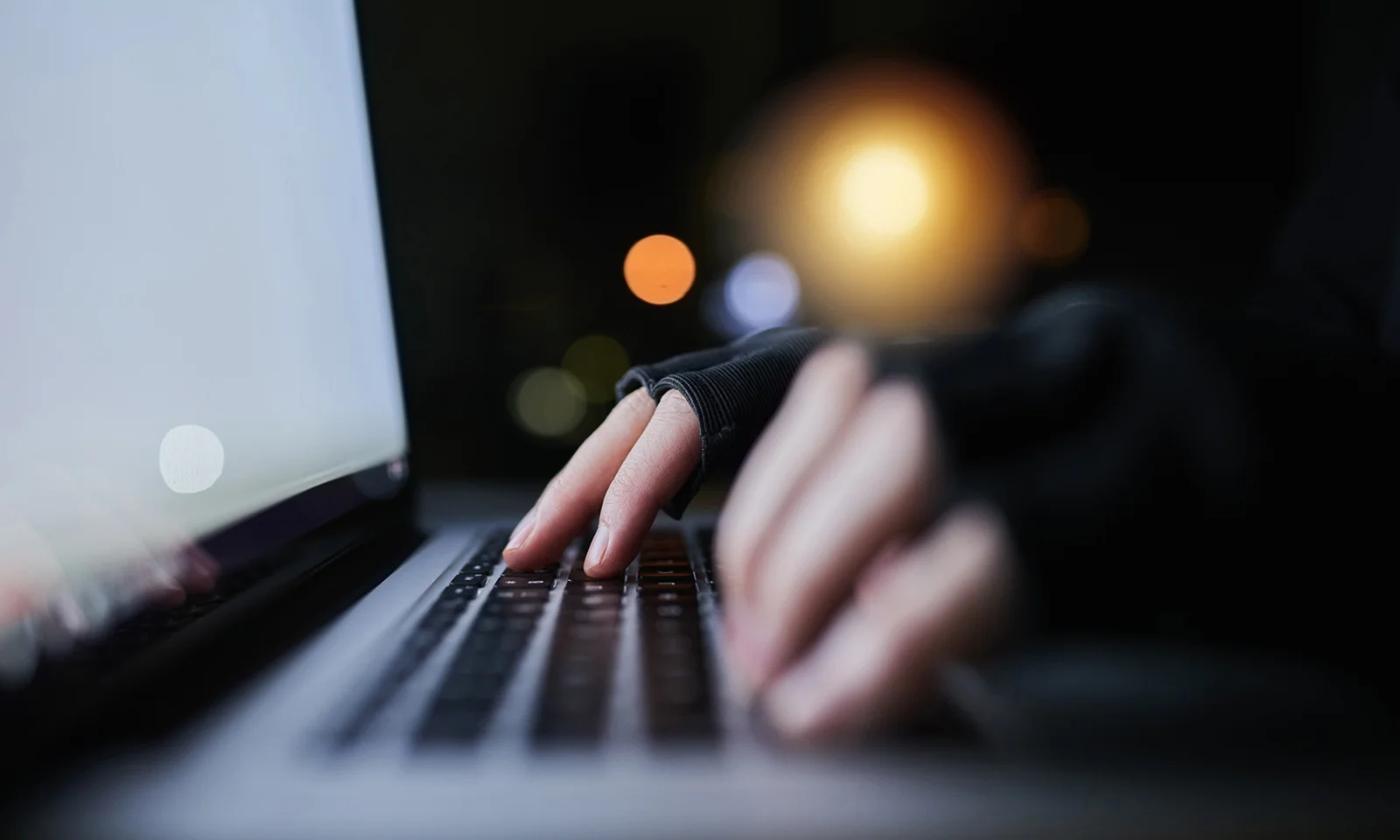 Close-up of hands typing on a laptop keyboard in a dimly lit environment, symbolising the use of AI and big data to combat fraud.