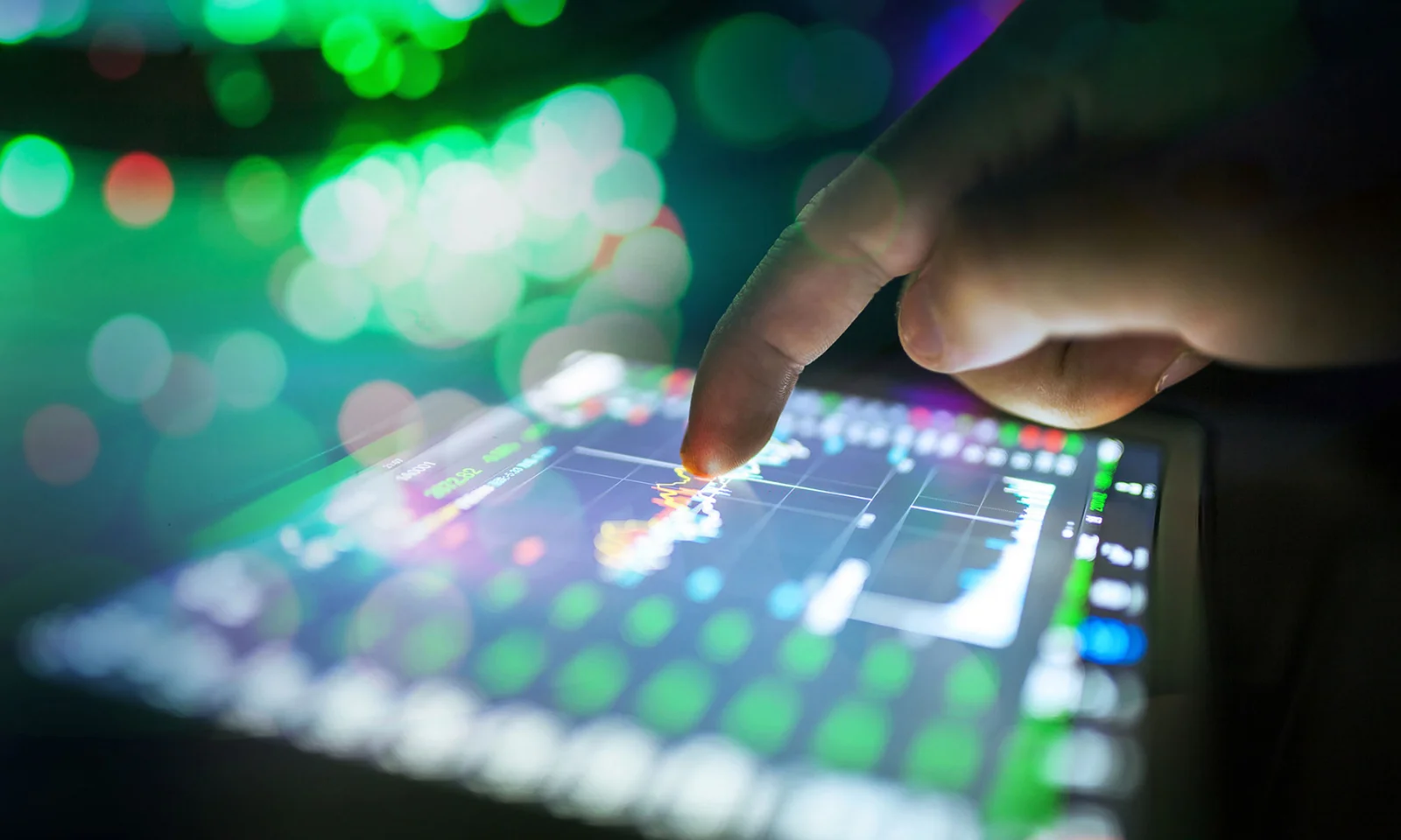 Close-up of a finger interacting with a touchscreen displaying energy management data, with vibrant green and colorful bokeh lights in the background.