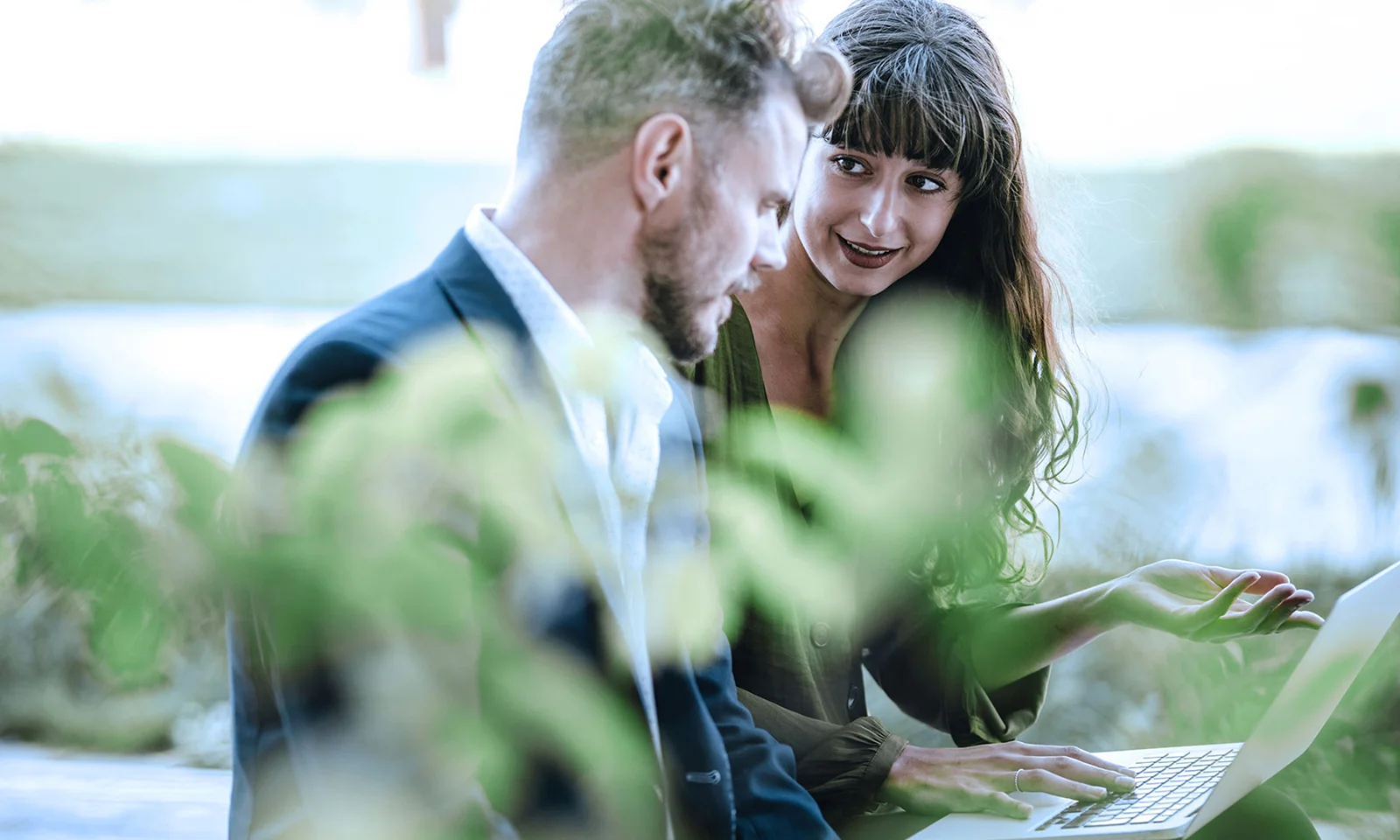 A man and a woman engaged in a focused discussion outdoors, with lush greenery surrounding them, symbolizing transparency and ethics in business practices.