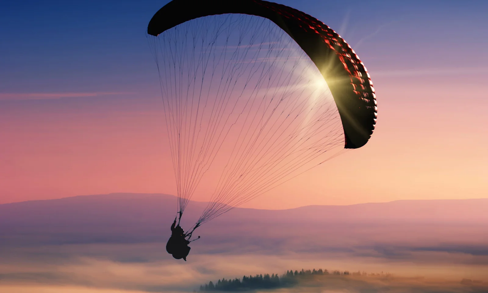 A breathtaking silhouette of a paraglider soaring through a vibrant sunset sky, symbolising the freedom, agility, and expansive possibilities offered by hybrid and multicloud solutions.