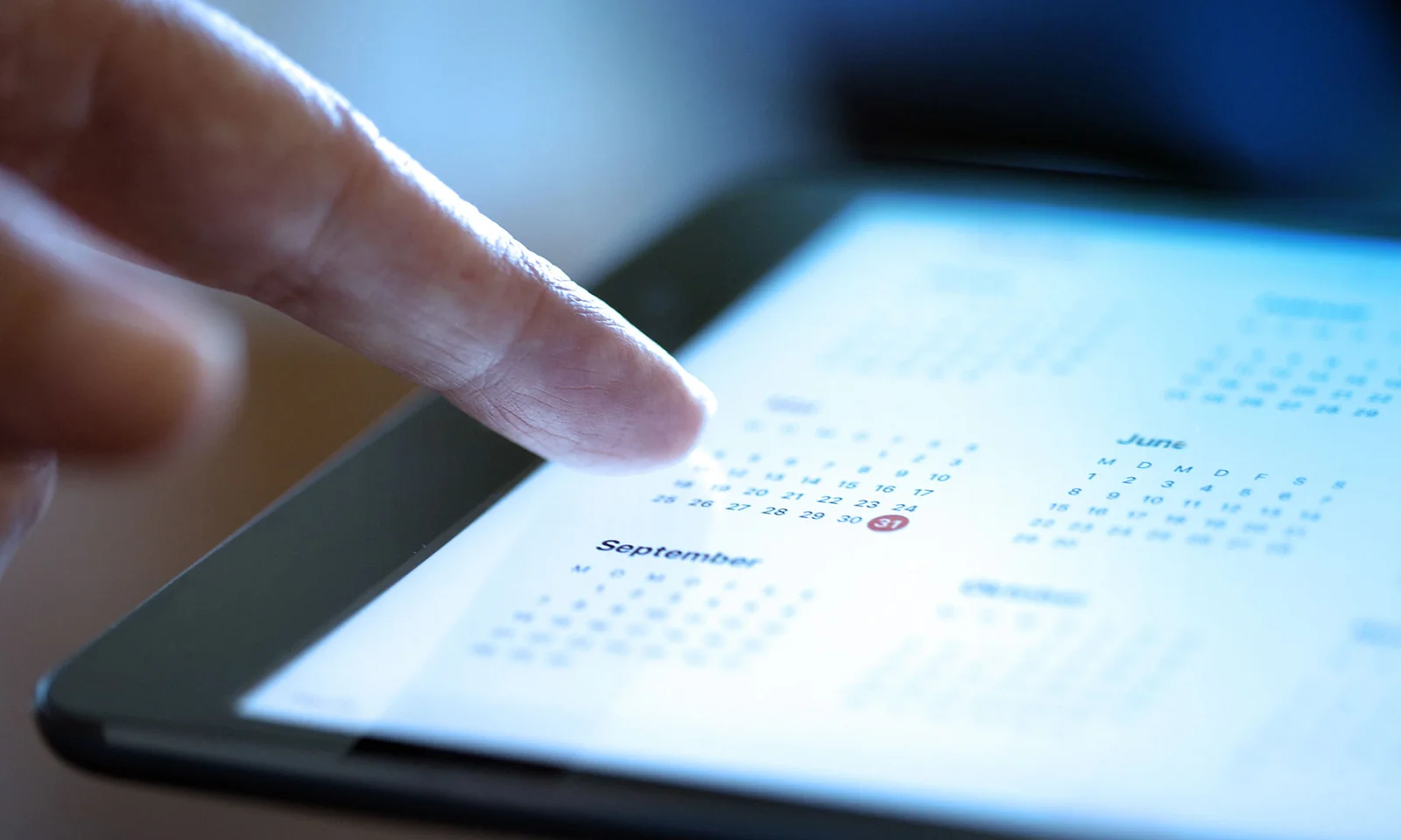 A close-up of a hand interacting with a digital calendar on a tablet, highlighting a date, symbolizing important financial and scheduling events.