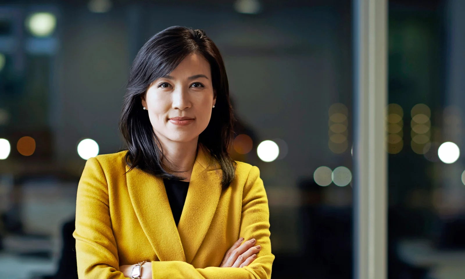 Confident professional woman in a yellow jacket with arms crossed, representing executive leadership.