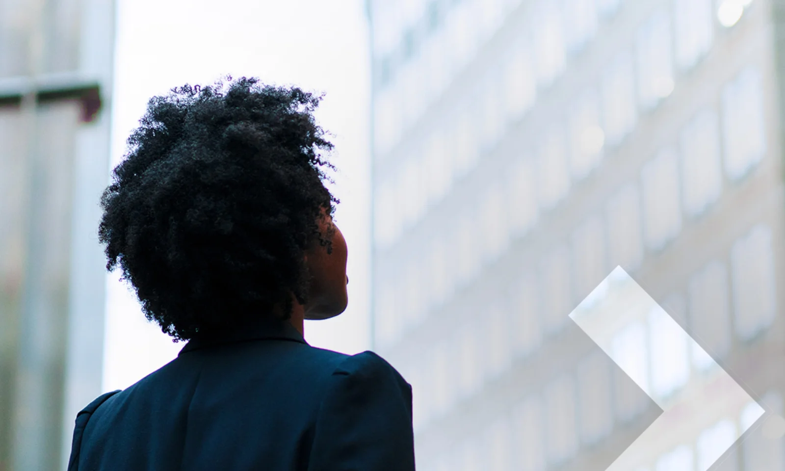 Eine Person mit lockigem Haar blickt auf moderne Bürogebäude, die eine professionelle und zukunftsorientierte Perspektive symbolisieren.