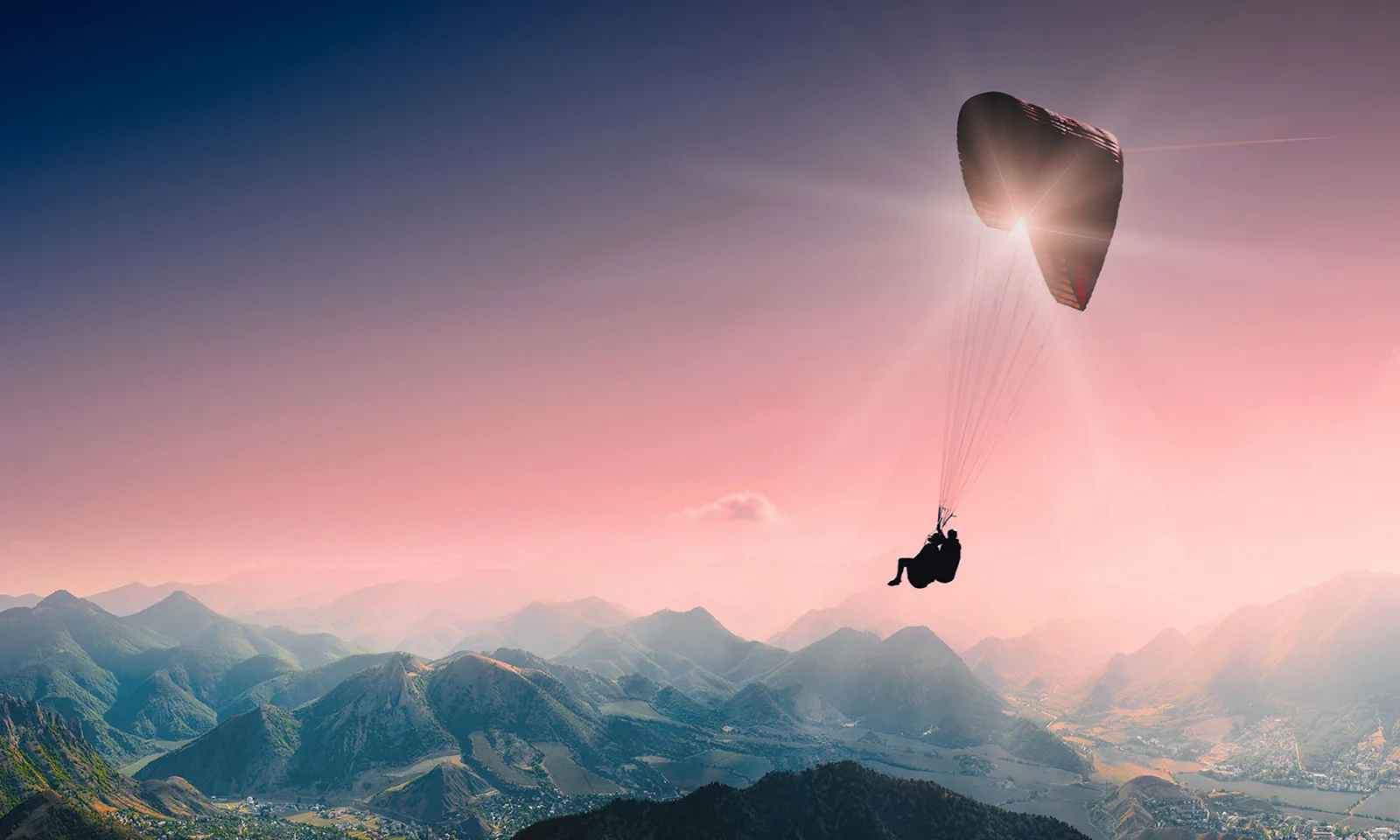 A paraglider floating above a vast landscape of mountains at sunset, symbolising the expansive opportunities and freedom provided by GFT’s cloud technology solutions.