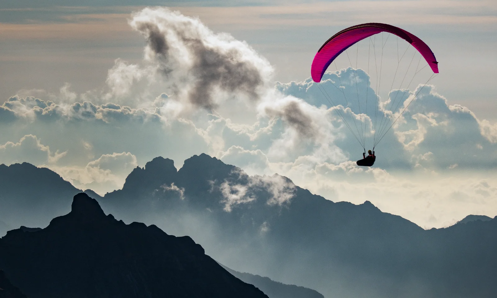 Gleitschirmflieger umgeben von Bergen und Wolken, verwendet als Key Visual für Cloud Services und Consulting.