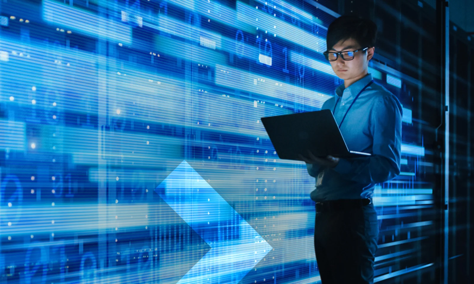 Ein junger Mann mit Brille arbeitet an einem Laptop in einem Serverraum. Im Hintergrund sind leuchtende, horizontale Linien und Datenströme zu sehen, die technologische Prozesse und digitale Transformation symbolisieren.