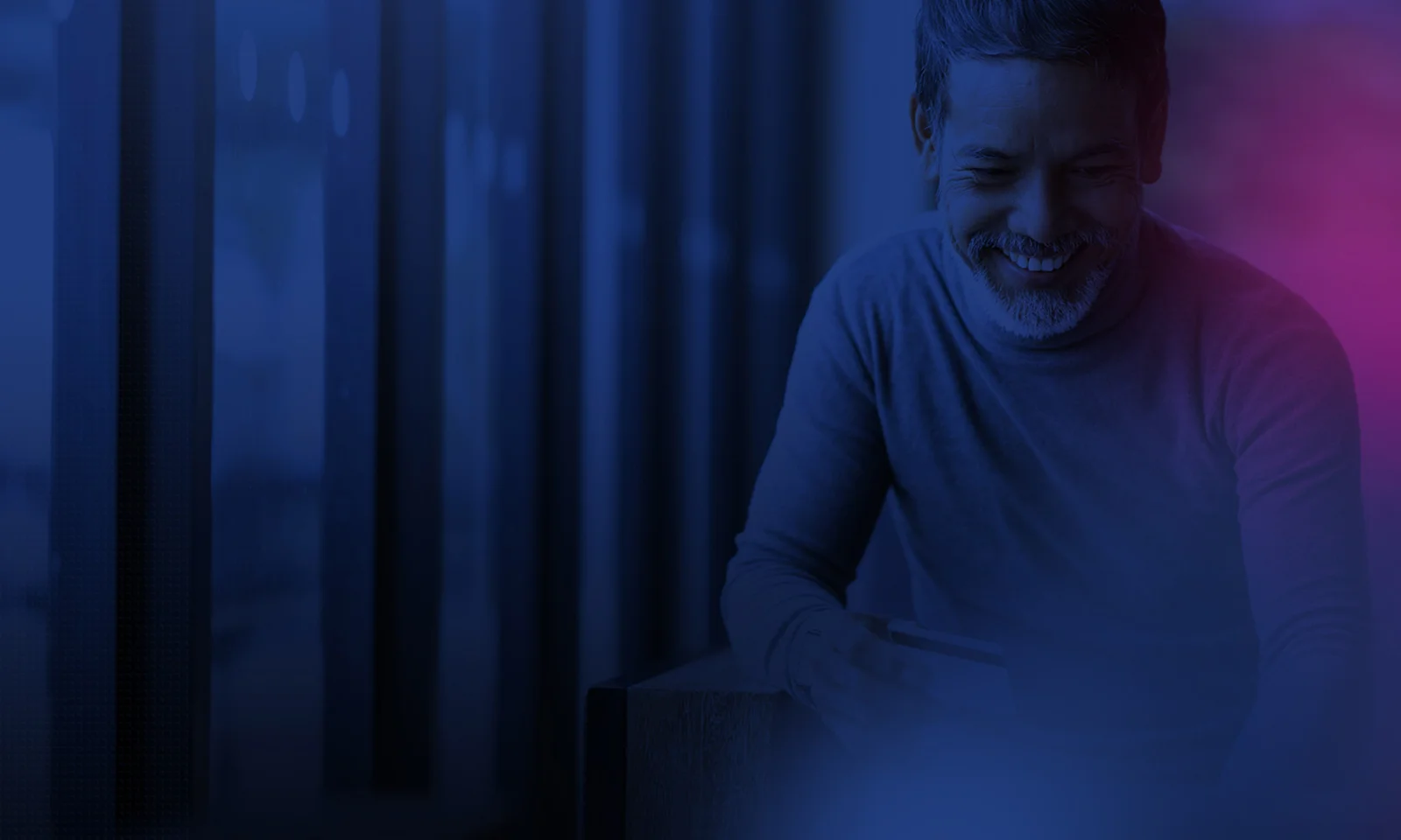 A man smiling while holding a credit card, making an online payment in a dimly lit, modern setting.