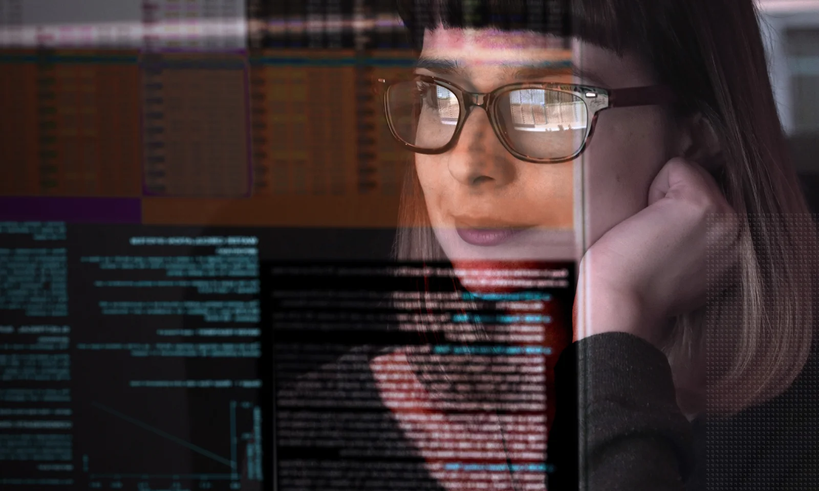 A woman wearing glasses intently looks at multiple programming screens with lines of code and data reflected in her glasses, representing software development and data analysis.