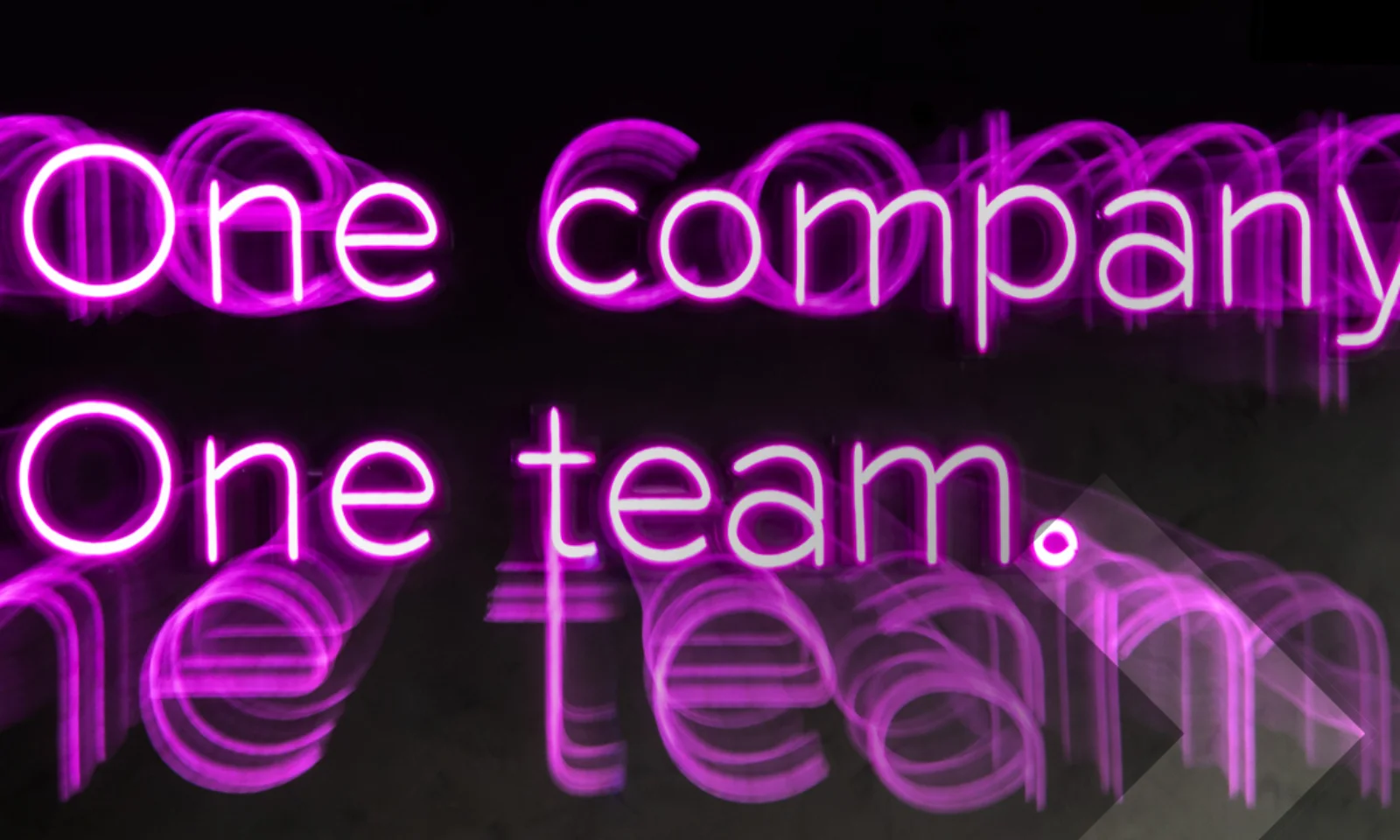 Neon sign with the words &quot;One company. One team.&quot; in vibrant pink, emphasizing unity and collaboration within an organization.