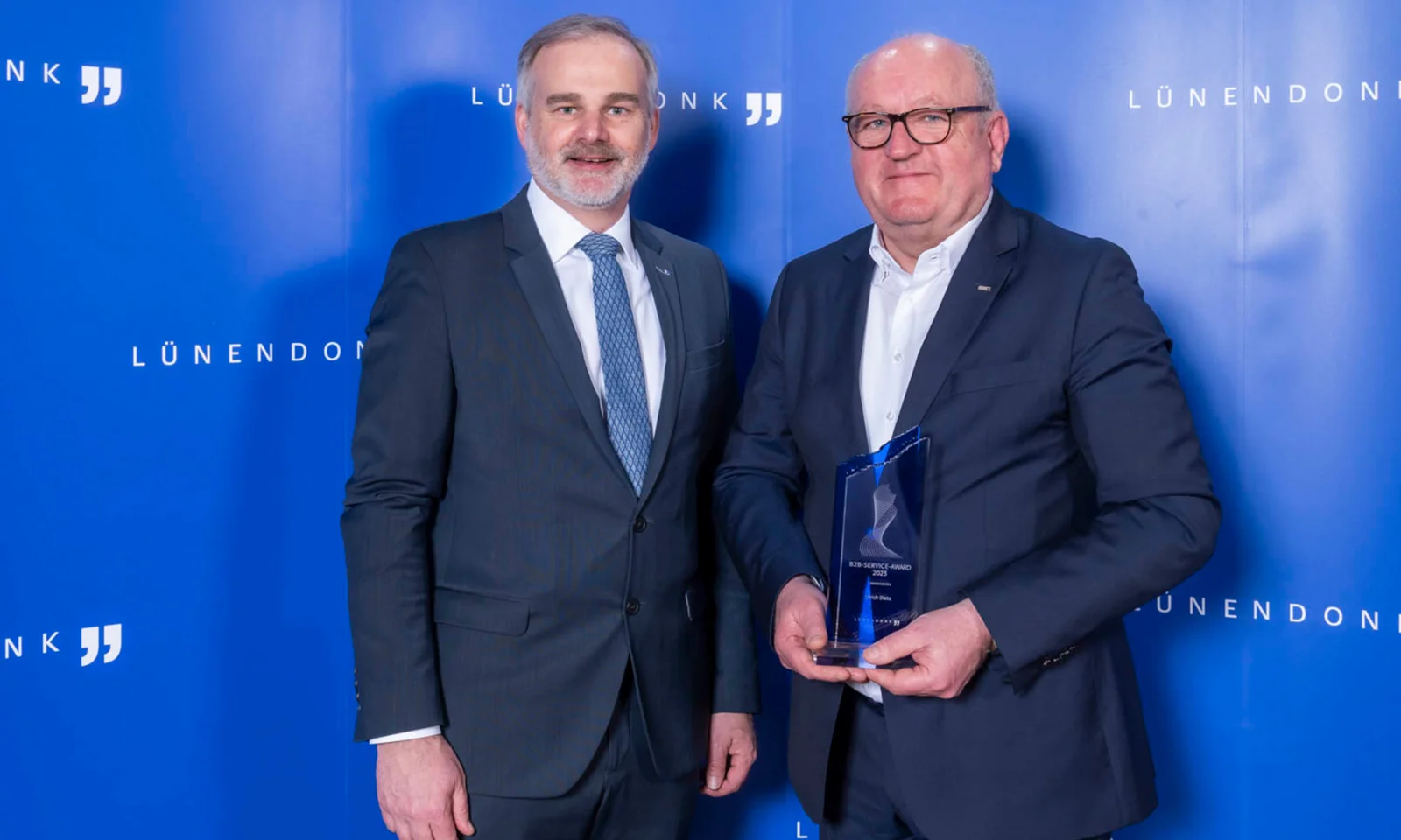 Ulrich Dietz and a colleague holding the Lünendonk B2B Service Award at an award ceremony, standing in front of a blue backdrop.