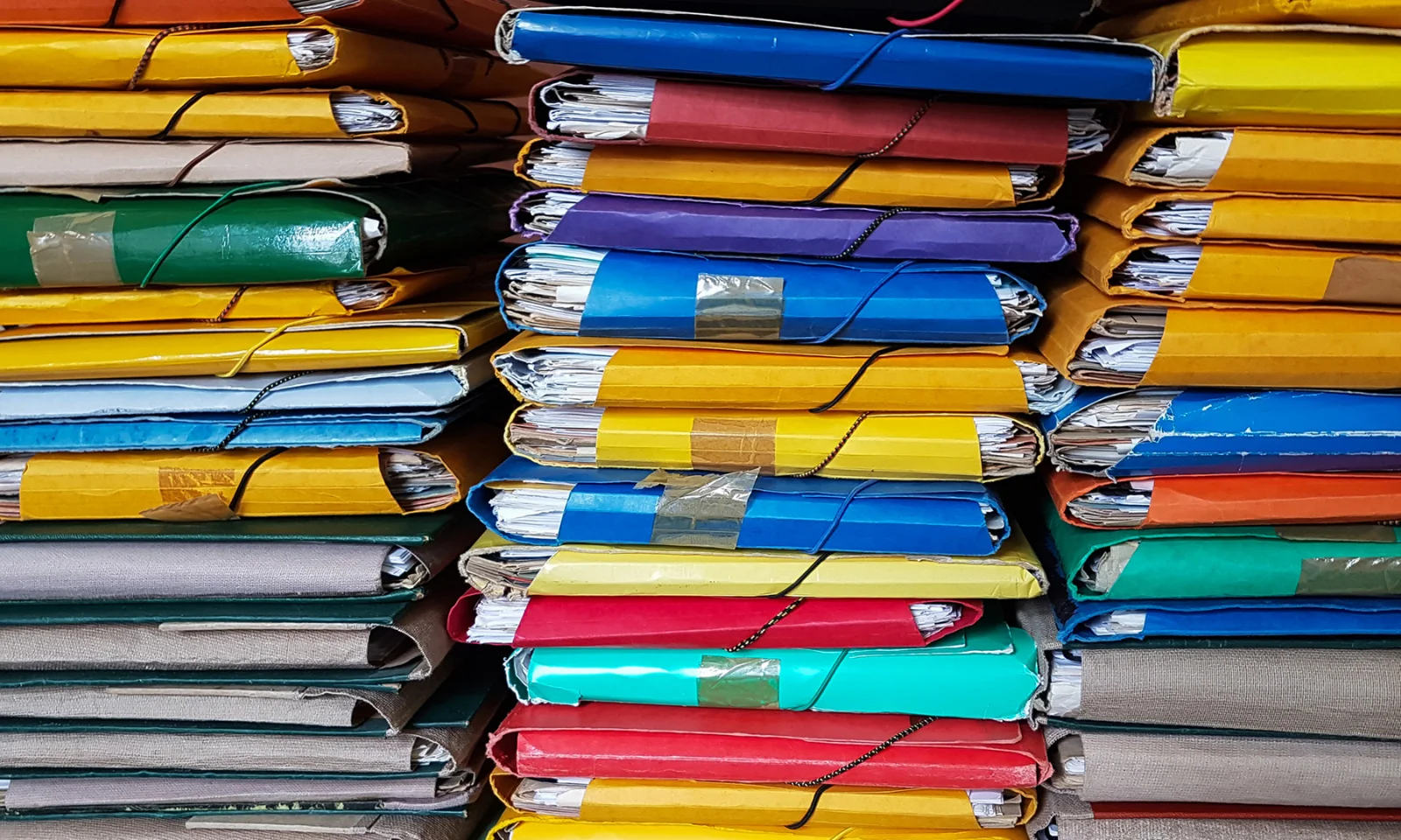 Stacks of colourful, overstuffed folders representing disorganised data storage.