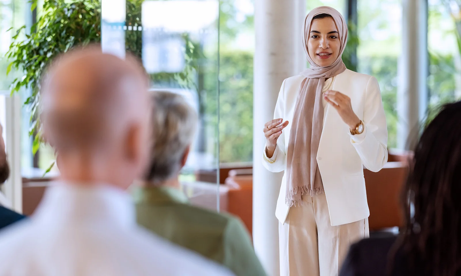 A confident woman in a headscarf presenting to a diverse group, embodying GFT&#039;s commitment to culture and values in a professional setting.