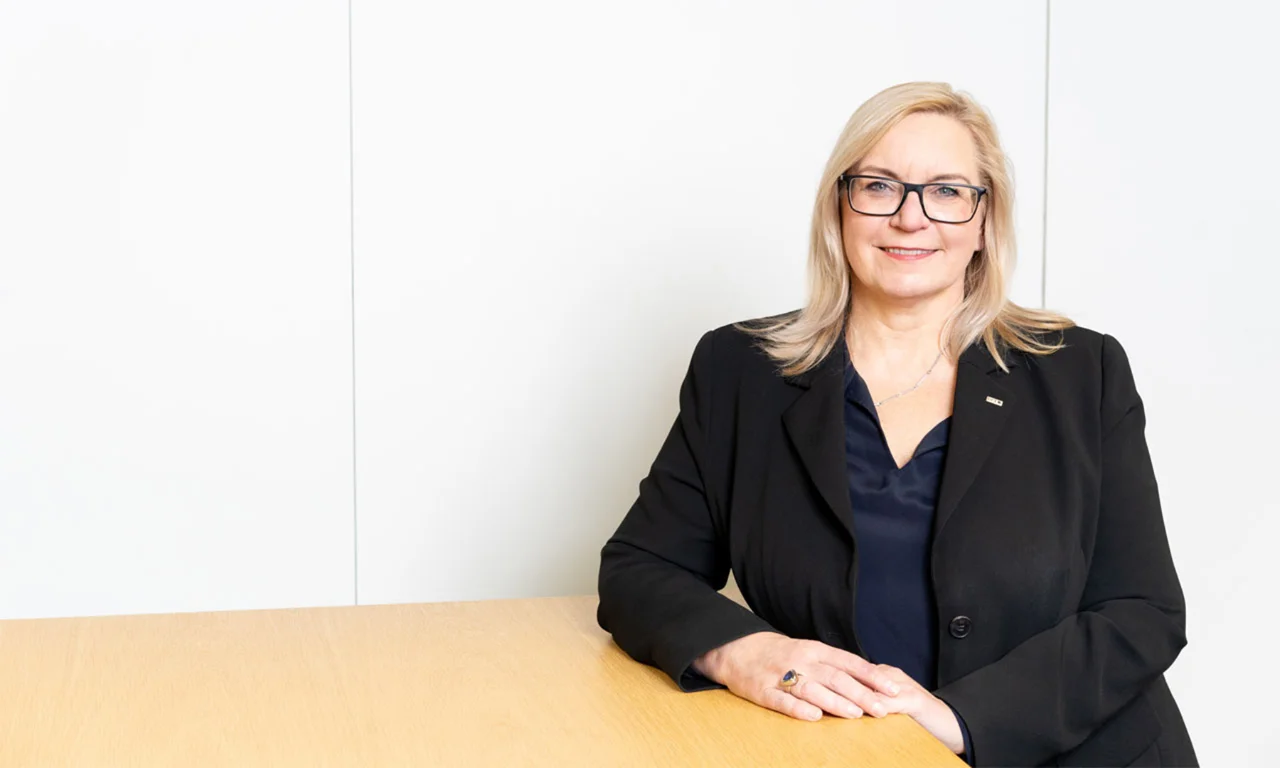 Marika Lulay, a member of the GFT Administrative Board, seated at a table wearing a black blazer and glasses, representing executive leadership and professionalism in the technology industry.