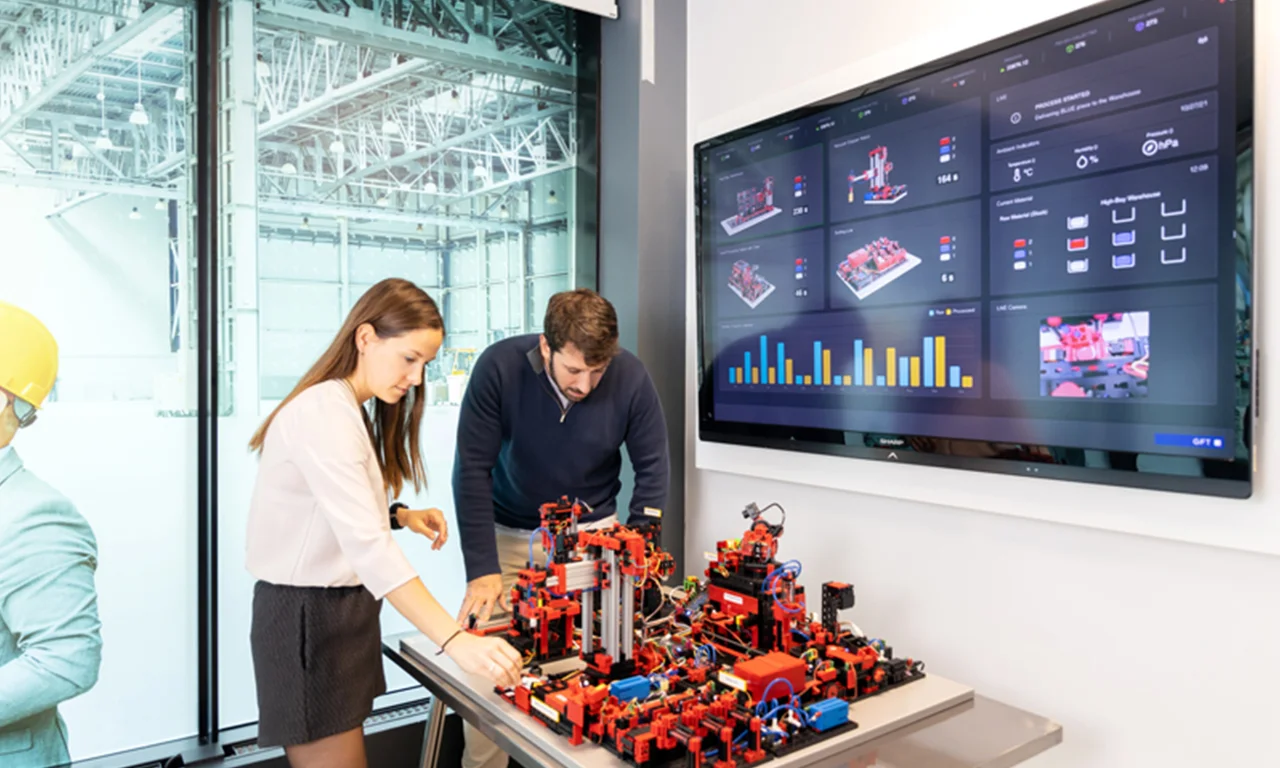 Two professionals collaborating in an innovation lab, utilizing industrial automation technology and real-time data analytics displayed on a large screen.