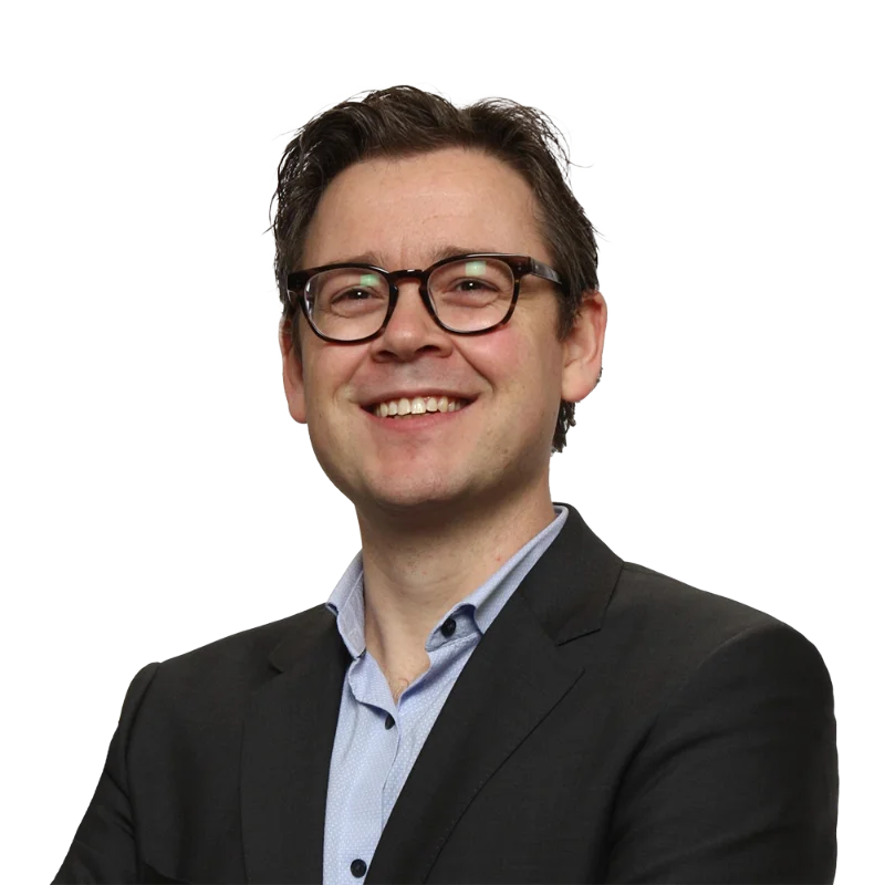 Portrait of Mathieu Liabaud wearing glasses and a dark suit while smiling.